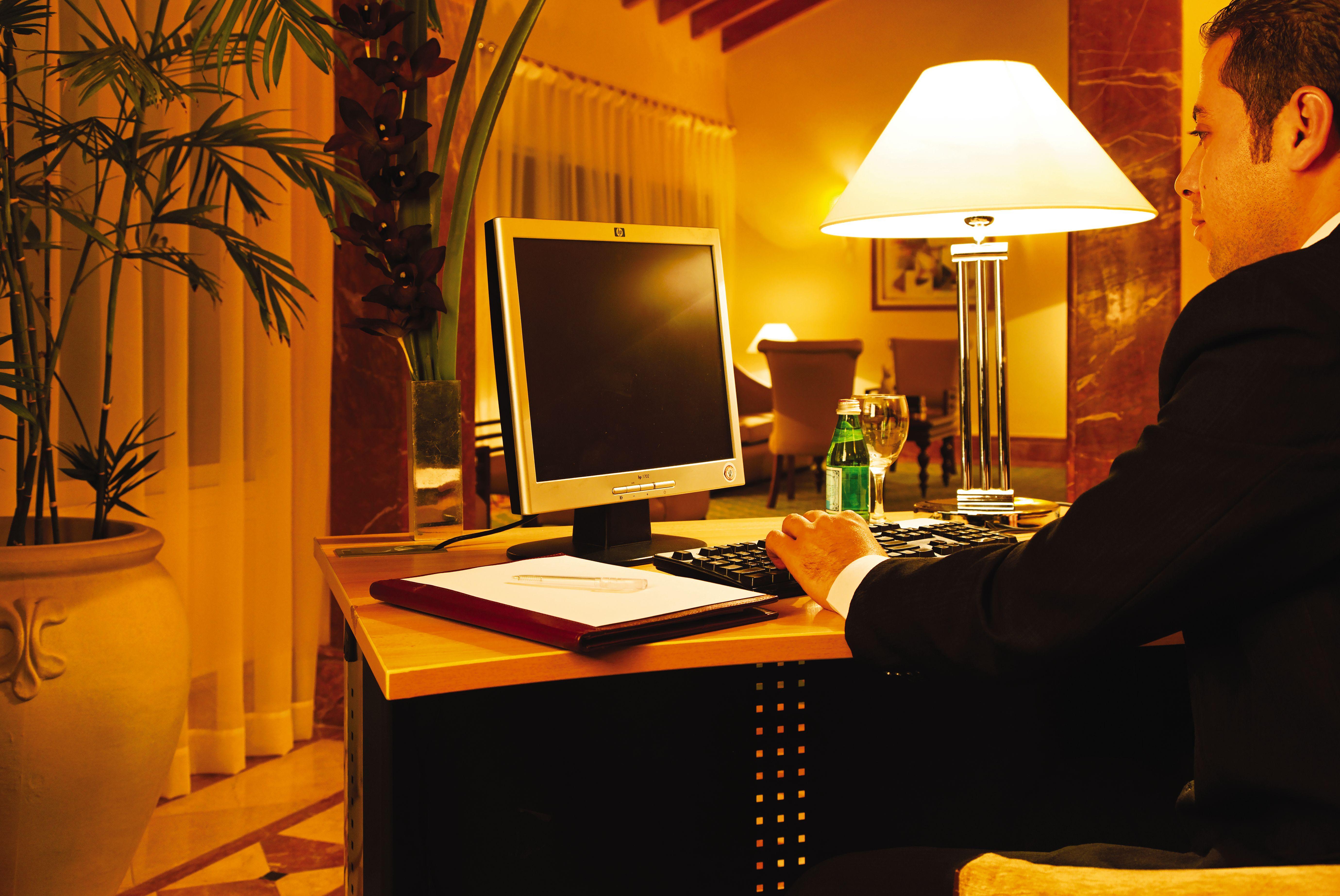 Movenpick Taba Resort & Spa Exteriér fotografie The photo shows a workspace with a desk and a computer. The desk is positioned in a well-lit area, with soft lighting coming from a nearby lamp. A person, dressed in a suit, is seated at the desk, using the computer. Next to the computer, there is a 